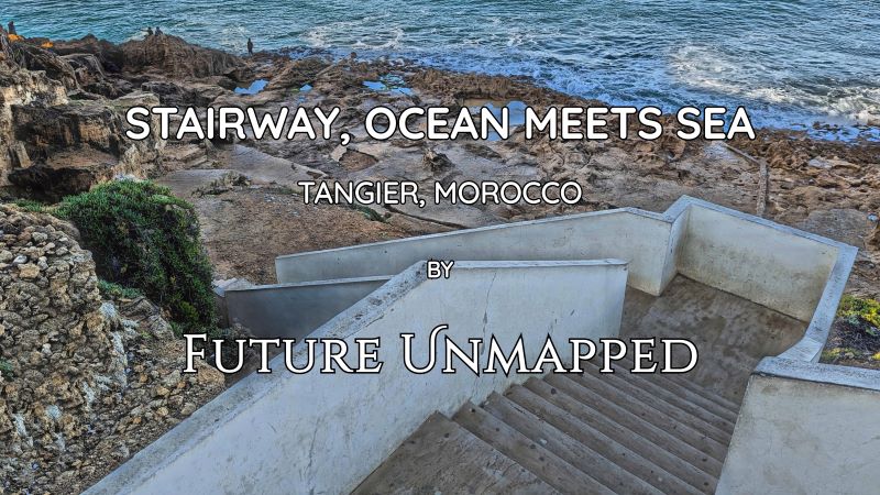 Rough, eroded, rocky coastal shoreline - with weathered, white-walled, staired pathway - stretches along vast, blue-green, panoramic expanse of water.