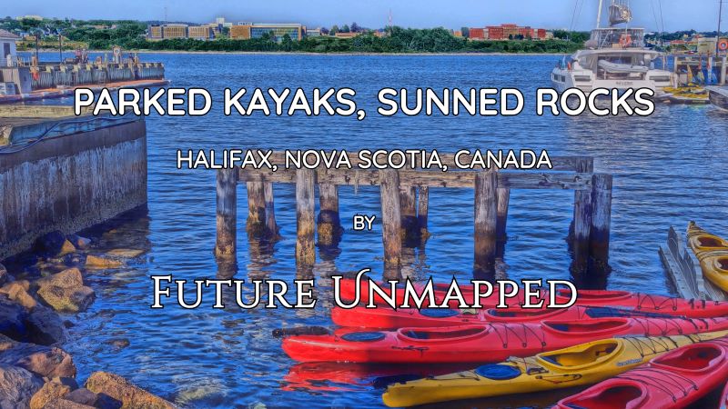 Mixed collection of kayaks docked in shallow, rocky area - along capital city waterfront boardwalk - facing local community college across harbour.