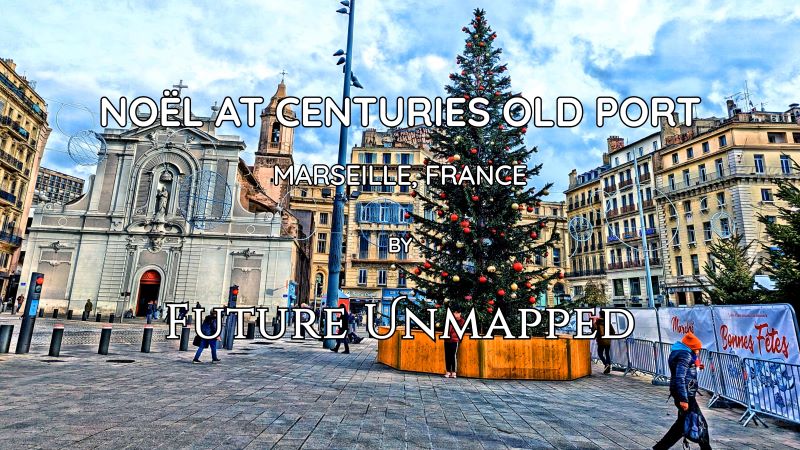 Large, decorated Christmas tree - surrounded by light-stoned buildings and bell-towered church - towers over wintry pedestrianized market square with festive banner.